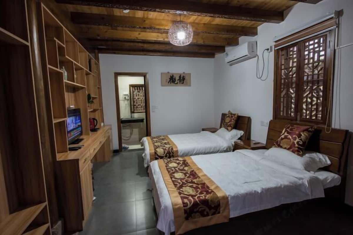 Une chambre avec deux lits, des étagères en bois, une télévision et un paravent décoratif traditionnel.