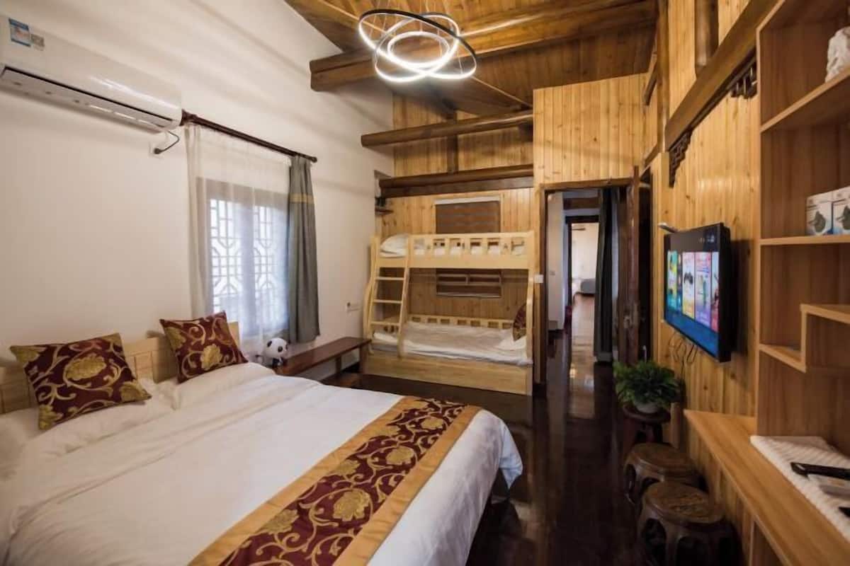 Une chambre avec un lit superposé, un lit simple agrémenté d’oreillers à motifs, un téléviseur fixé au mur et un plafond en bois.