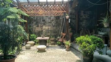 A stone-floored patio with a wooden swing set, potted plants, and a hanging plant.