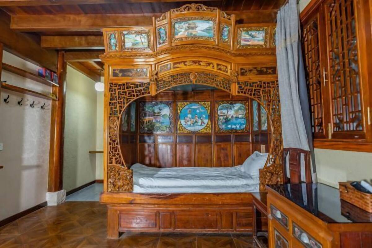 Un lit traditionnel en bois, orné de sculptures et de peintures complexes, une armoire en bois avec un miroir, et une porte en bois avec un motif en treillis.