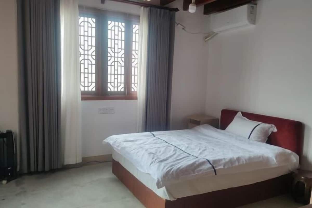 Une chambre à coucher avec un lit, des rideaux, une fenêtre ornée d’une grille décorative et un appareil de climatisation.