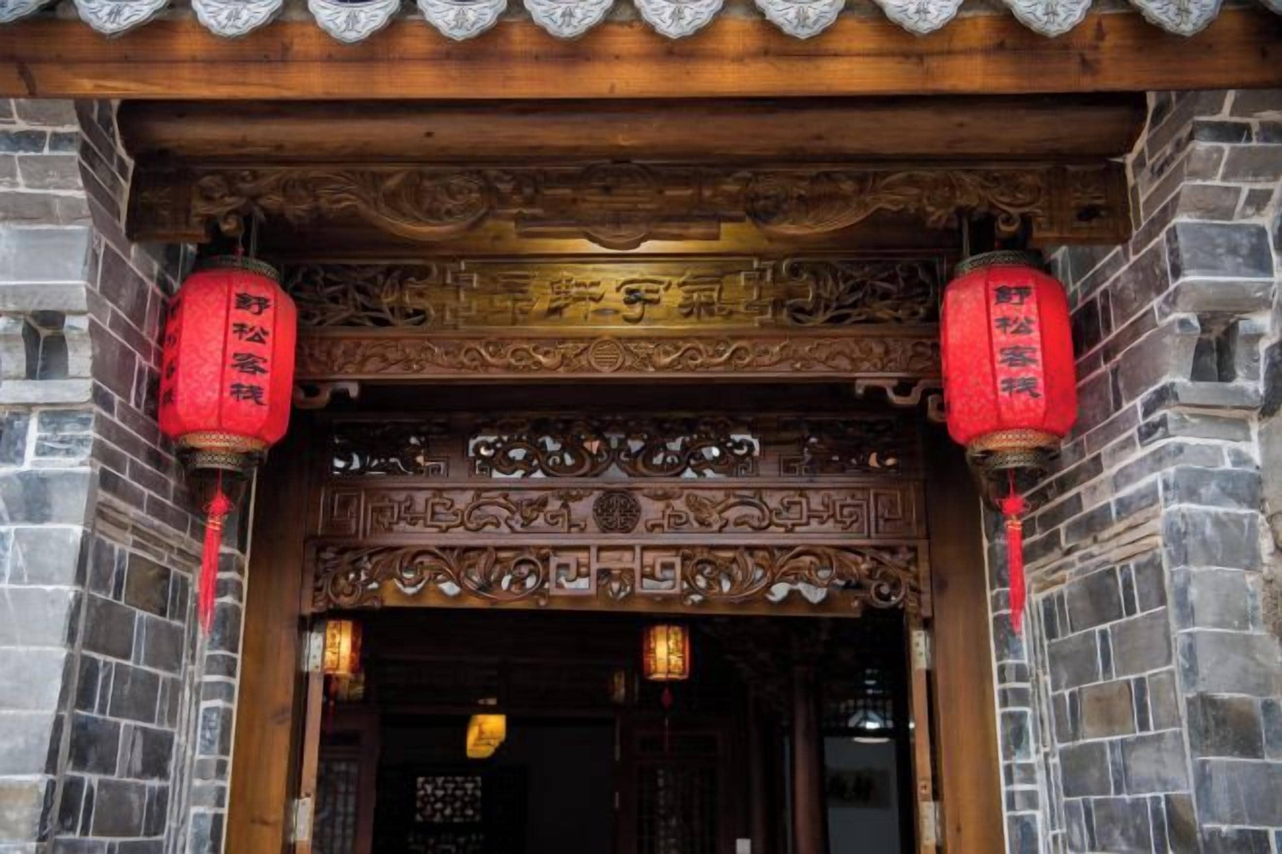 A traditional wooden entrance with intricate carvings and red lanterns.