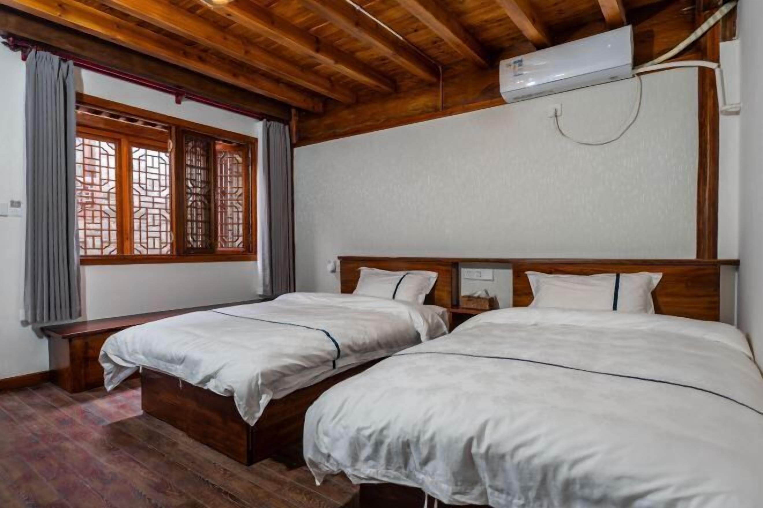 Quarto com duas camas, vigas de madeira, janela com padrão de treliça tradicional e ar condicionado.