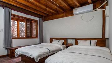 Quarto com duas camas, vigas de madeira, janela com padrão de treliça tradicional e ar condicionado.