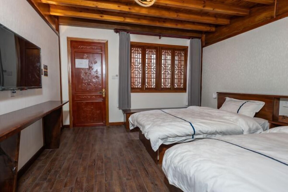 Una habitación con suelo de madera, una puerta de madera, un ventanal de diseño tradicional y dos camas con ropa blanca.