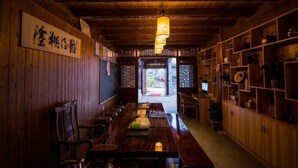 Interior de madeira tradicional com uma longa mesa de jantar, prateleiras com diversos objetos e um lustre pendurado.