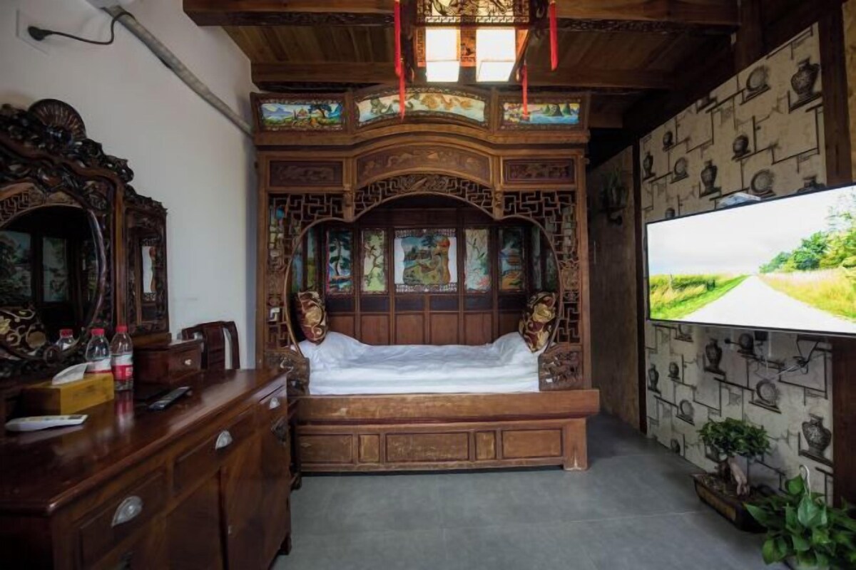 Una cama de madera tradicional con tallas elaboradas, un televisor de pantalla plana grande y un escritorio de madera con cajones.