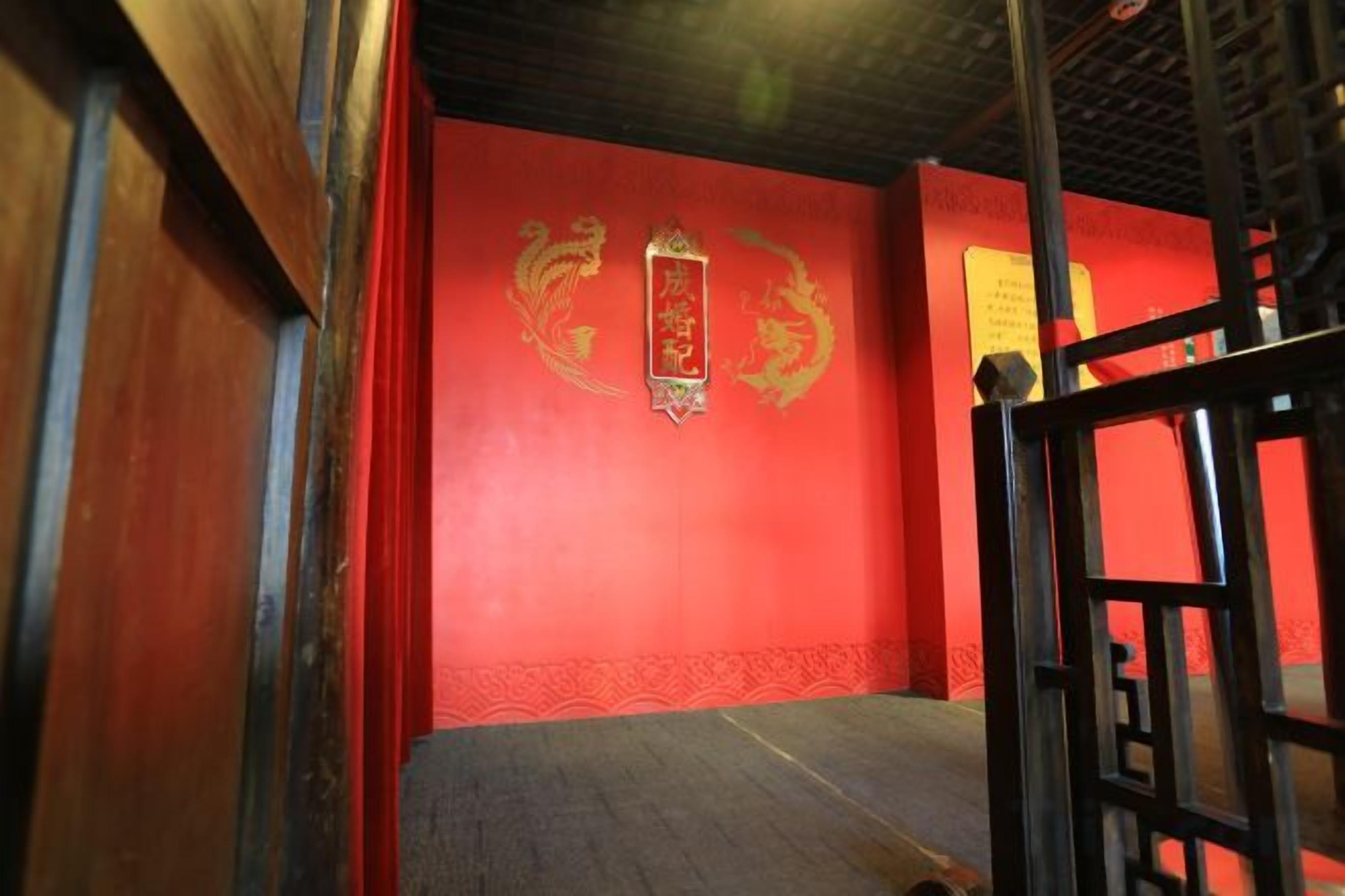 A room with a red wall, a wooden floor, and a black metal gate.