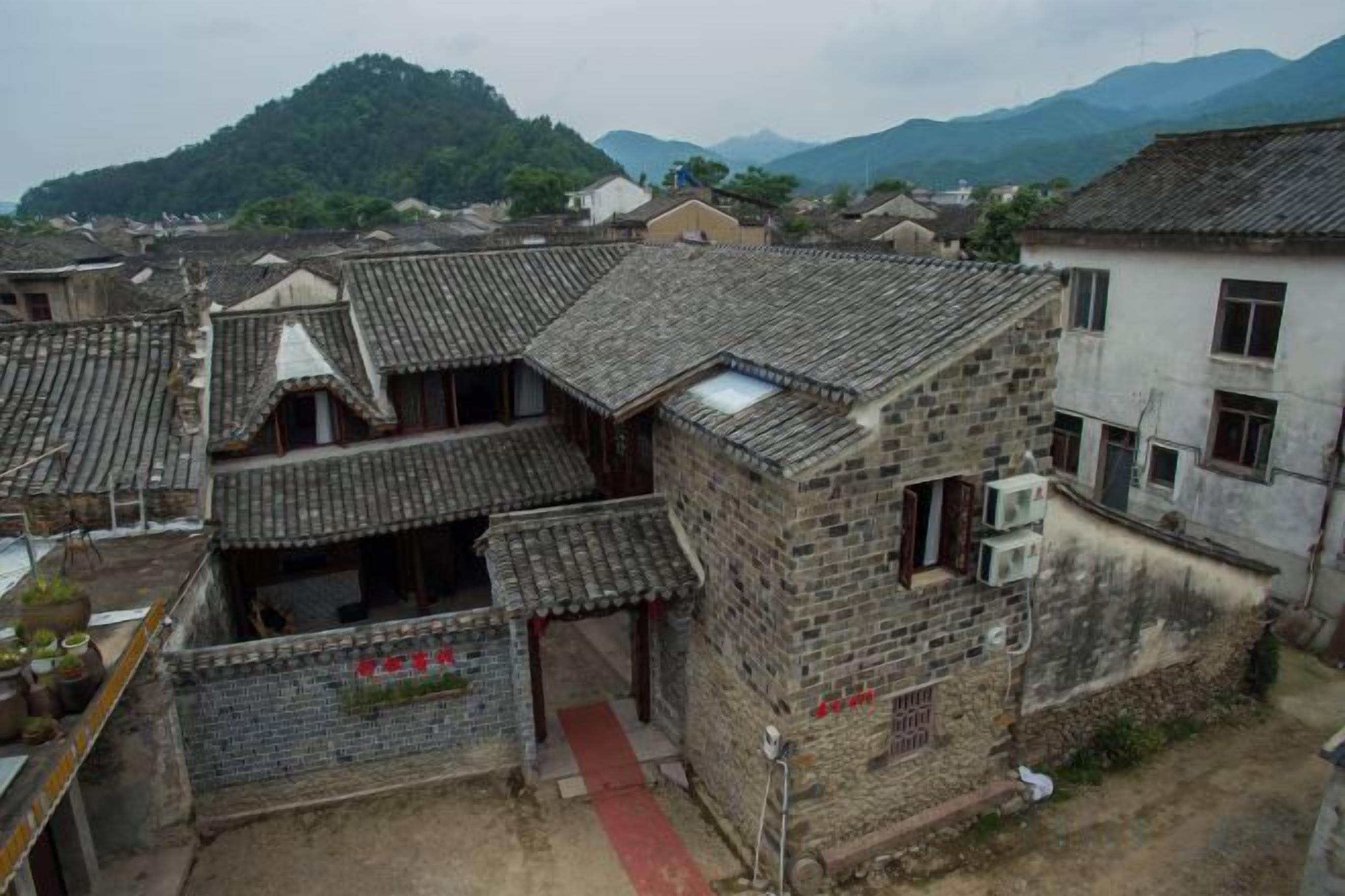 A traditional building with a tiled roof, a red pathway, and a mountainous backdrop.