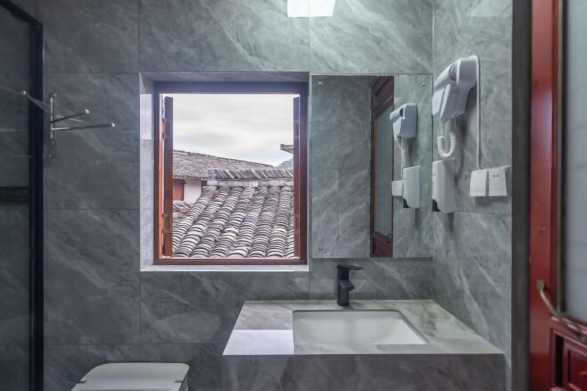 Un baño con pared de mármol, una ventana con vista a un tejado tradicional, un lavamanos y un inodoro.