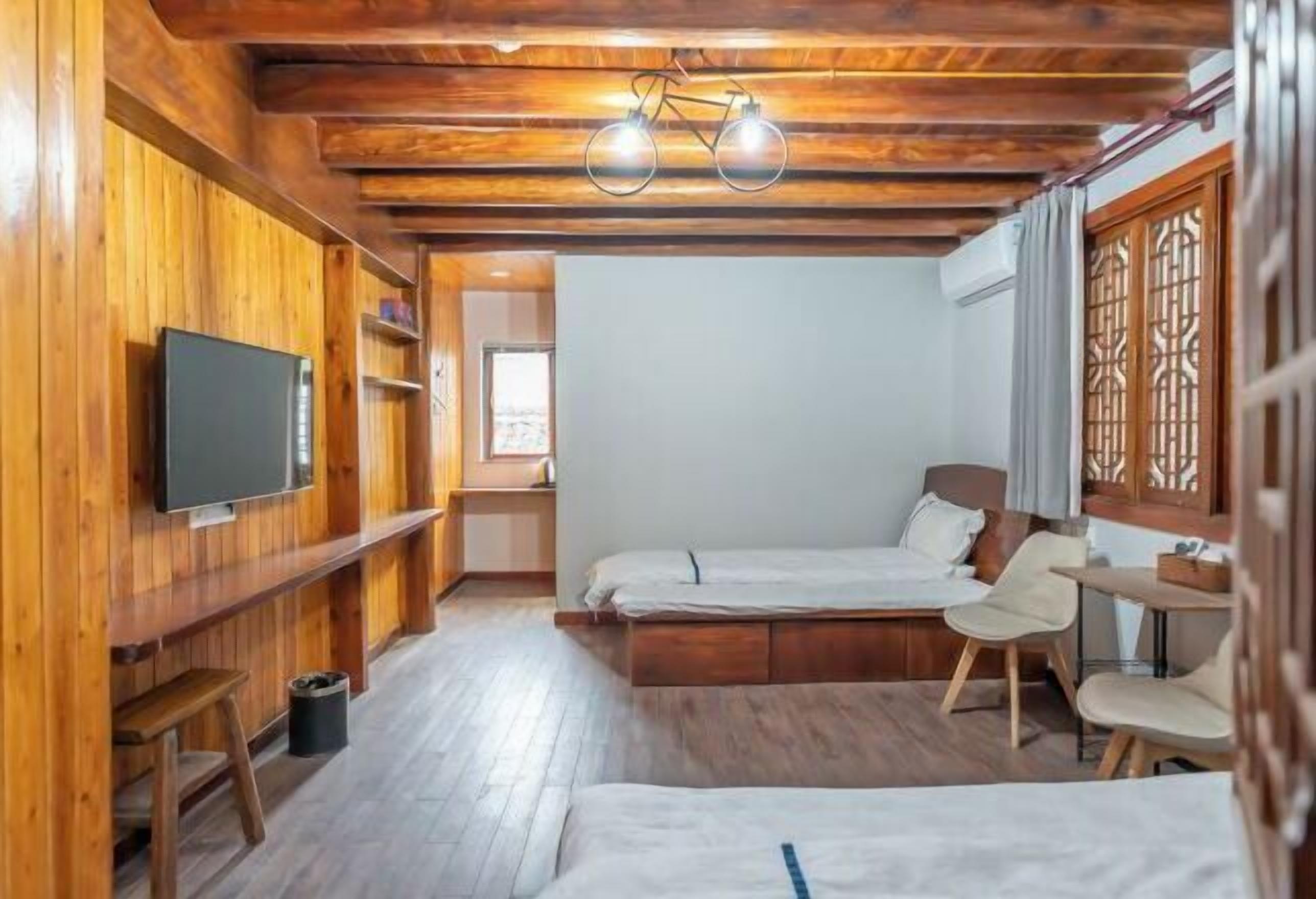 Quarto com painéis de madeira, uma cama, uma televisão, uma escrivaninha e uma cadeira.