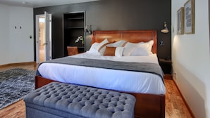 Une chambre à coucher moderne avec un grand lit, une tête de lit en bois, un pouf gris et un tapis noir et blanc.