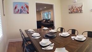 A dining area with a long wooden table set for six, surrounded by black chairs. There are two paintings on the walls, one depicting chickens and the other cows. - Kelly's Urban Farmhouse in Atlanta (Lithonia)