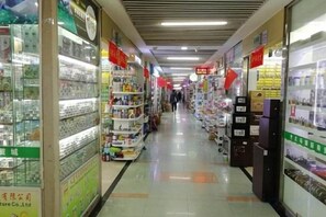 A corridor with shelves stocked with various products, signs indicating different sections, and a clean, tiled floor. - Anna Hostel (Yiwu)