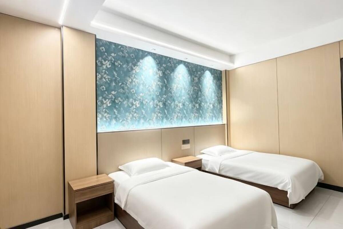 A modern hotel room with two beds, a nightstand, and a decorative wall panel.
