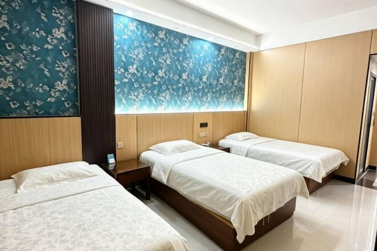 A hotel room with three beds, a wooden headboard, a large blue floral wall, and a modern design.