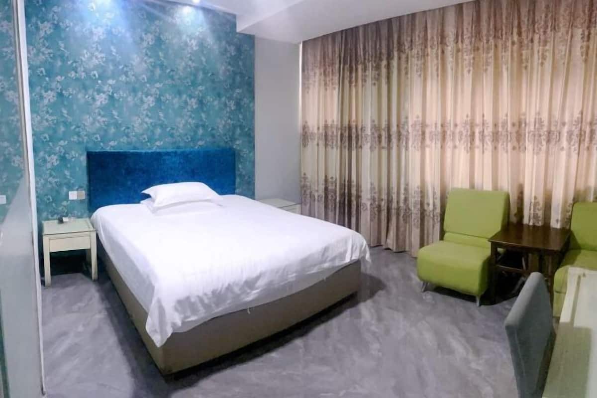 A hotel room with a bed, a nightstand, a green armchair, and a curtain.