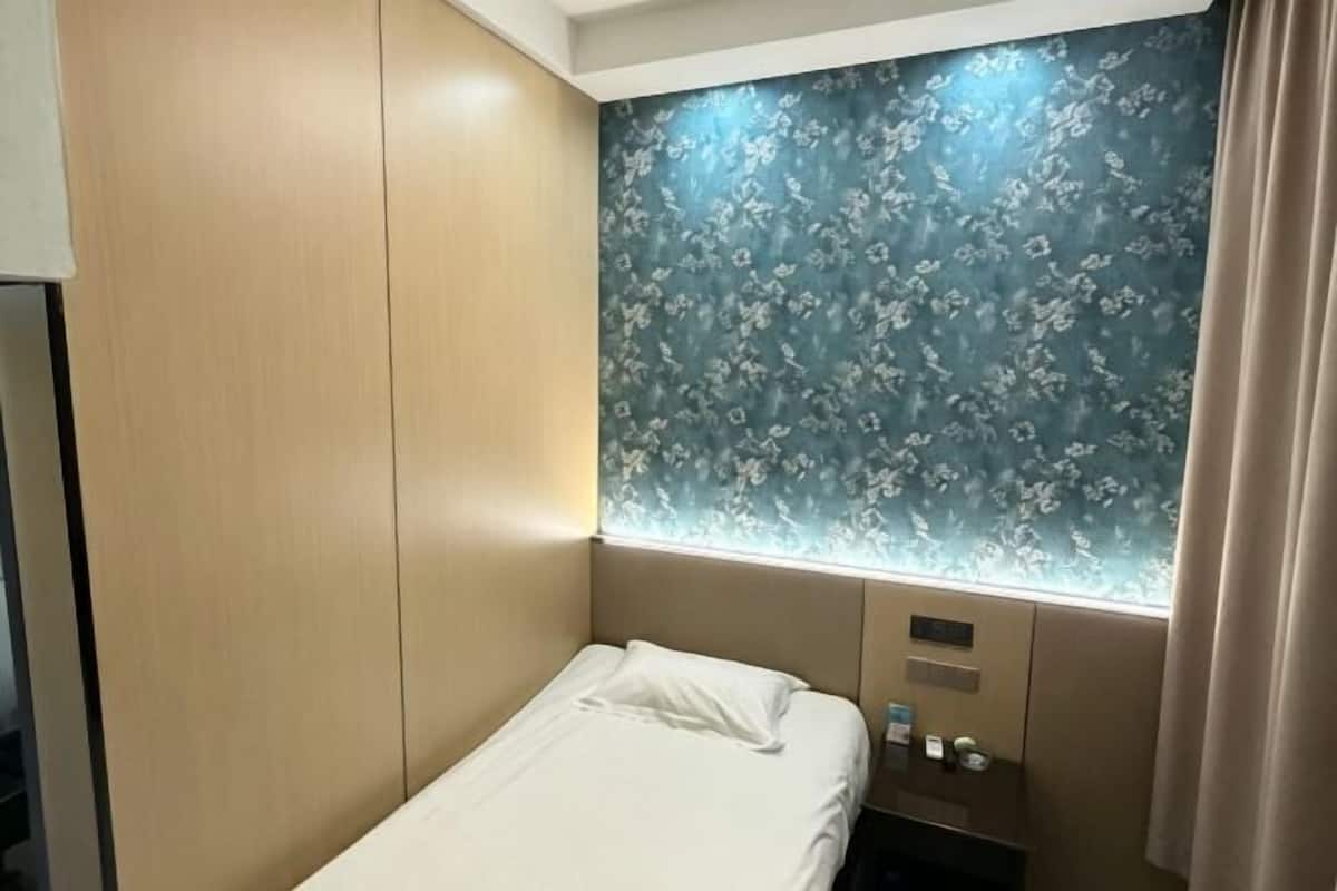 A hotel room with a bed, a nightstand, a wall-mounted light, and a floral-patterned wall.