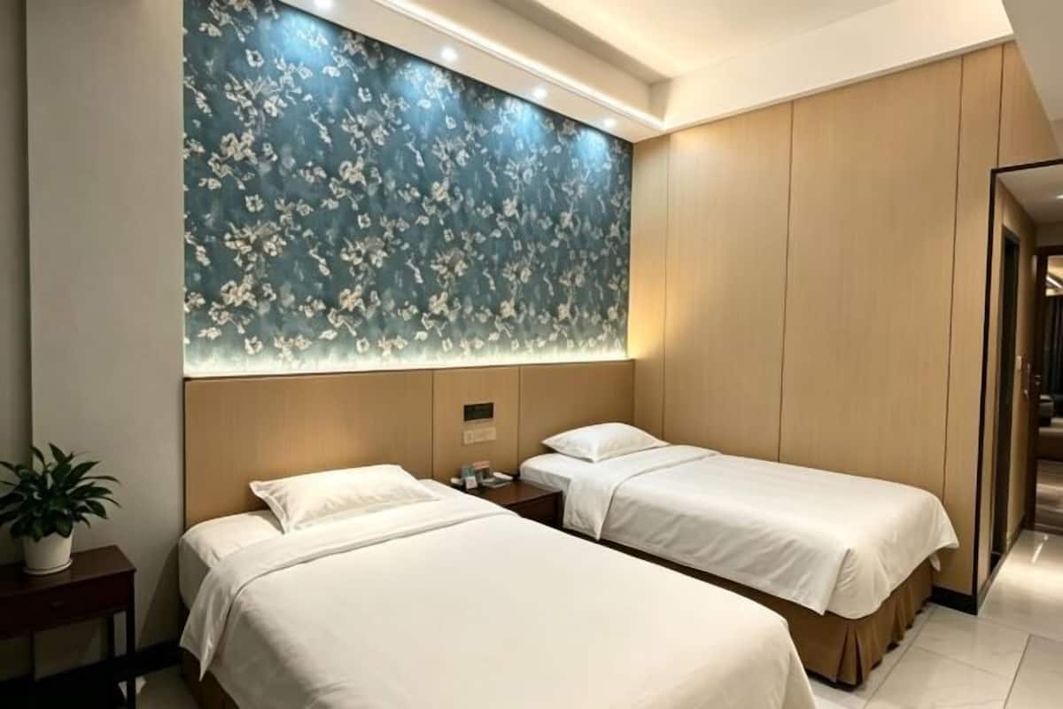 A hotel room with two beds, a floral wall, a potted plant, and a wooden panel wall.