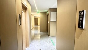 Un pasillo de hotel con un diseño limpio y moderno, que presenta un piso de mármol y paredes de madera. Se observan indicaciones con números de habitación y una señalización de salida.