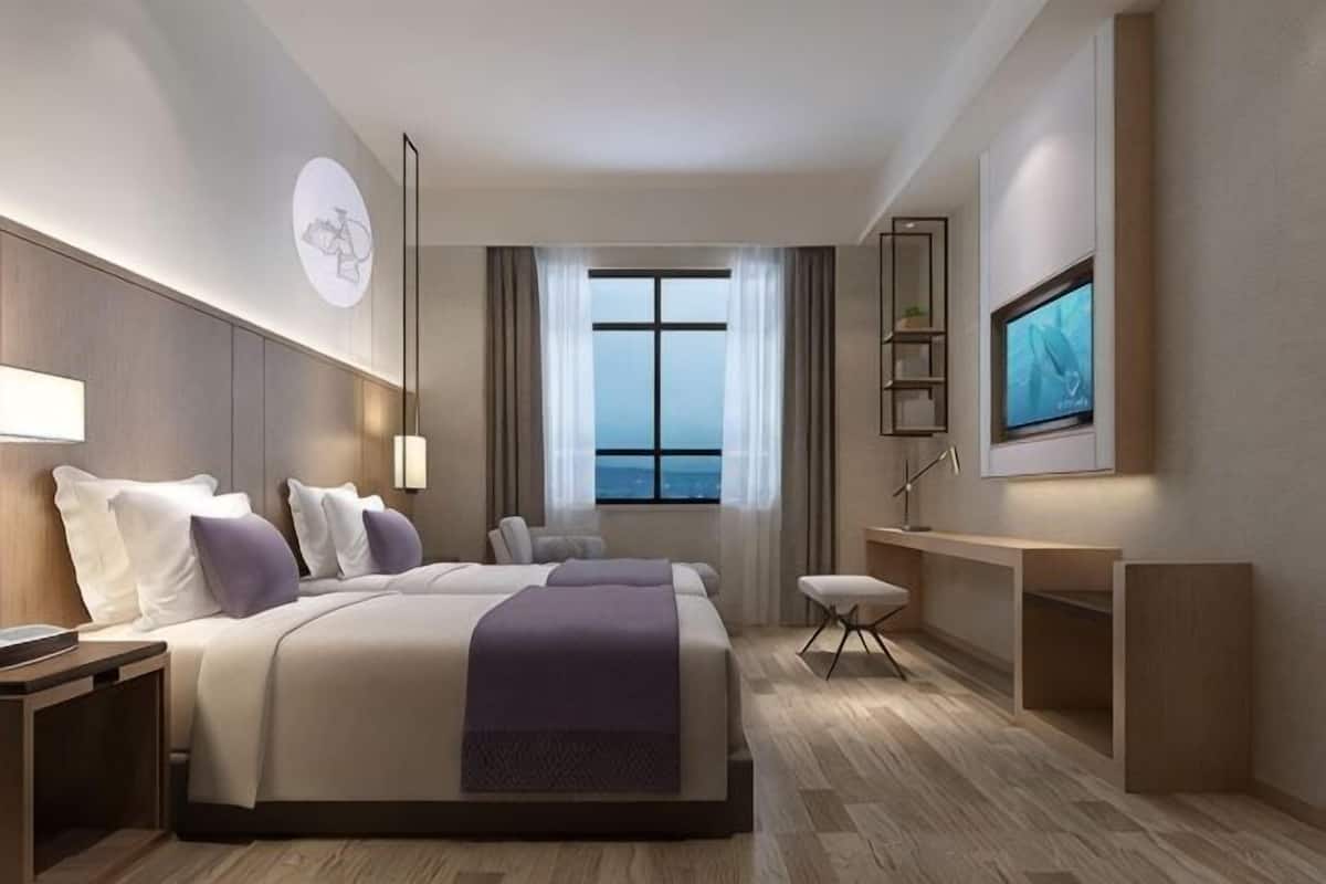 A modern hotel room with a large bed, a desk, a TV, and a view of the city.