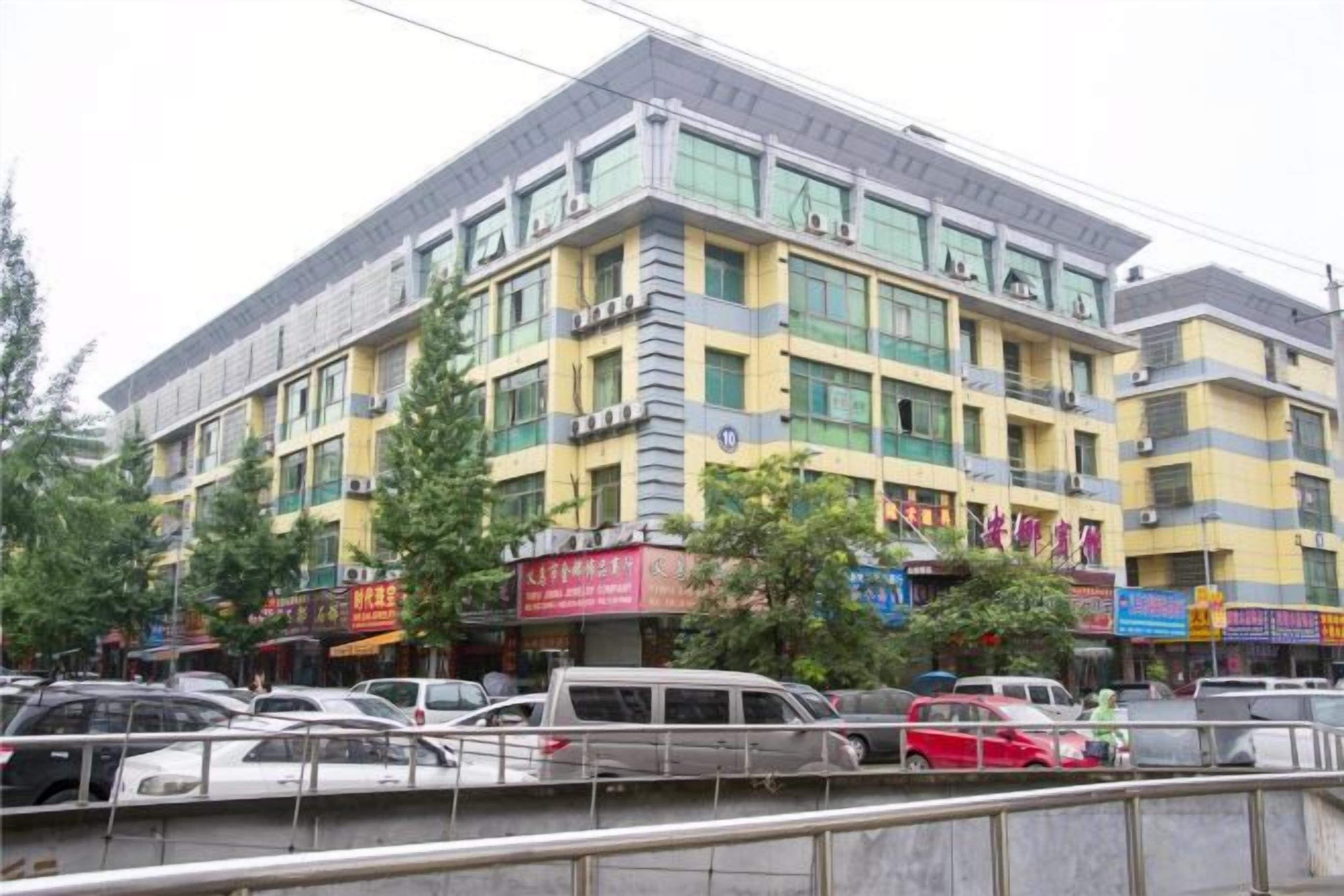 A multi-story building with commercial signage on the ground floor, surrounded by parked cars and trees.