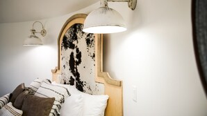 Une chambre à coucher avec un lit, deux lampes fixées au mur et un miroir avec un cadre en bois.