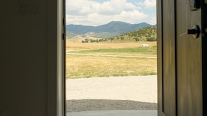 Une porte qui donne sur un champ verdoyant, avec des montagnes à l’horizon.