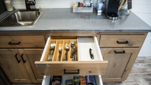 Une cuisine dotée d’un évier en acier inoxydable, de meubles de rangement en bois et d’un organiseur de tiroir contenant des ustensiles et des livres.