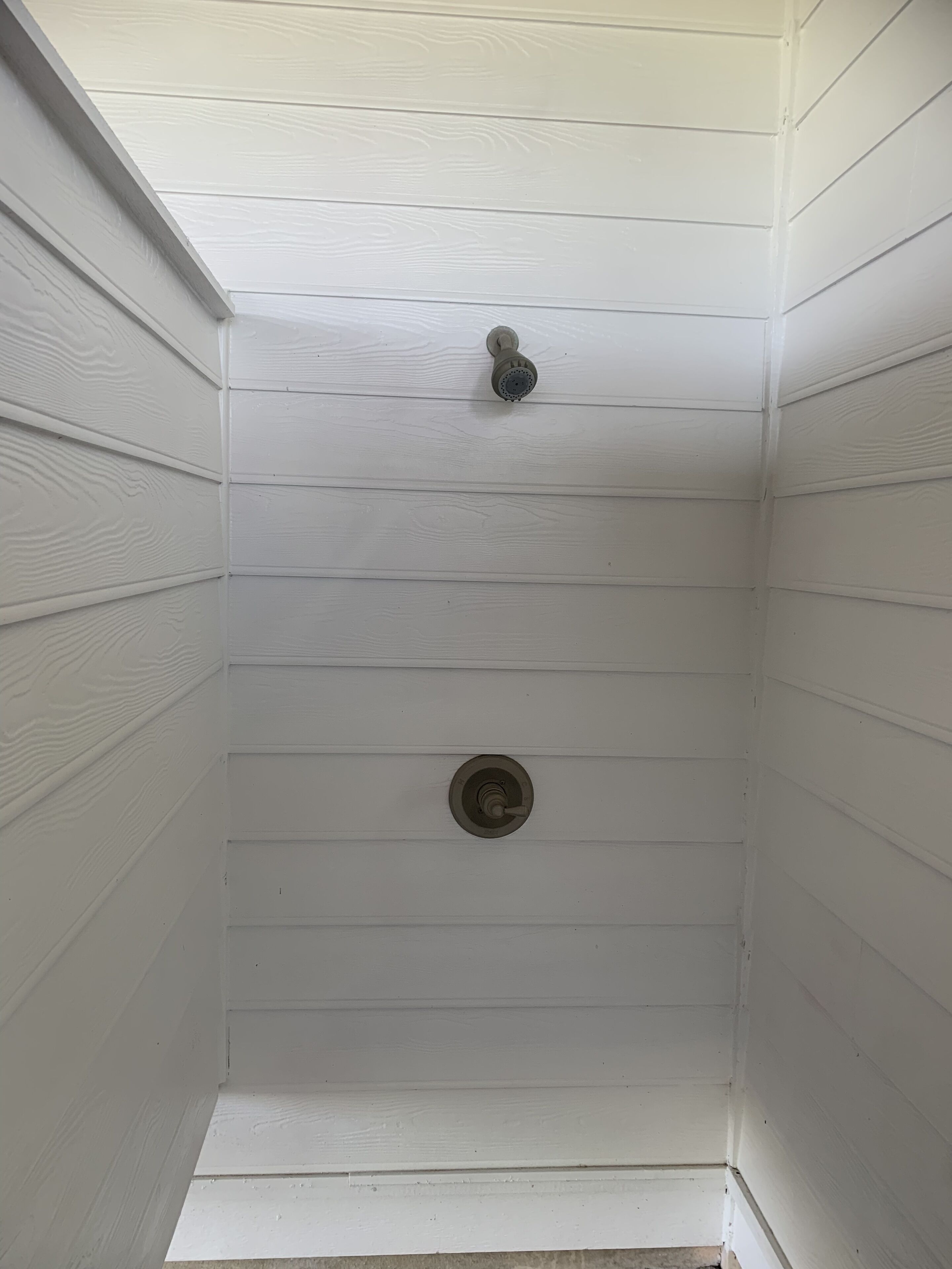 A small, white-paneled room with a single showerhead and a drain in the center.