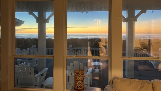 A room with large windows overlooking a deck with white chairs and a table.