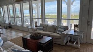 A spacious living room with a large window overlooking the beach, a cozy sofa set, and a wooden coffee table.