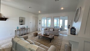 A spacious living room with a beige sofa, a coffee table, and a large window offering a view of the outdoors.