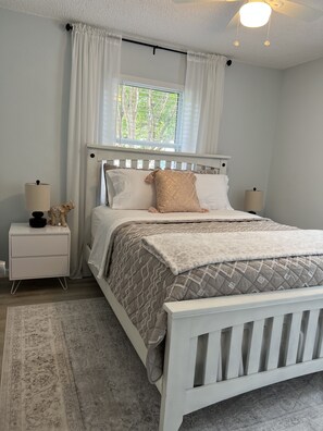 Quarto com cama, mesas de cabeceira, janela com cortinas e luminária no teto.