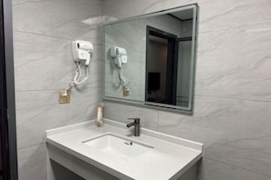 Un baño con un lavabo blanco, un espejo y dos secadores de pelo montados en la pared.