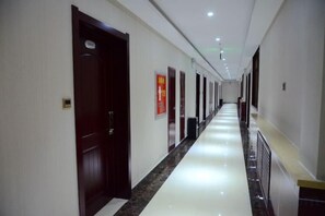 A hotel corridor with doors, a fire exit sign, and a trash bin. - Holiday Weekend Hotel (Xiahe)