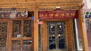 A traditional wooden building with intricate carvings and a sign indicating it is a hotel. - Holiday Weekend Hotel (Xiahe)