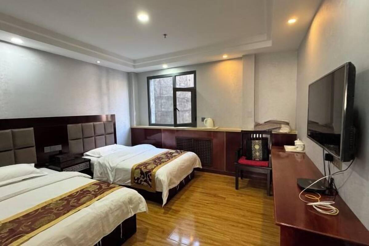A hotel room with two beds, a desk with a chair, a television, and a window.