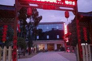 Un bâtiment traditionnel chinois doté d’une entrée en forme d’arc rouge, d’une façade moderne en verre et d’une cour intérieure avec des bancs.