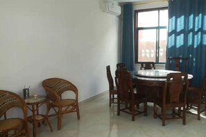 A dining area with a round table and chairs, a small side table with a lamp, and a window with blue curtains. - Baotianman Shanshui Inn (Neixiang)