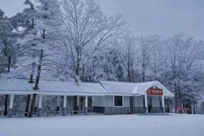 A building with a flat roof and a red sign, surrounded by snow-covered trees. - Baotianman Shanshui Inn (Neixiang)