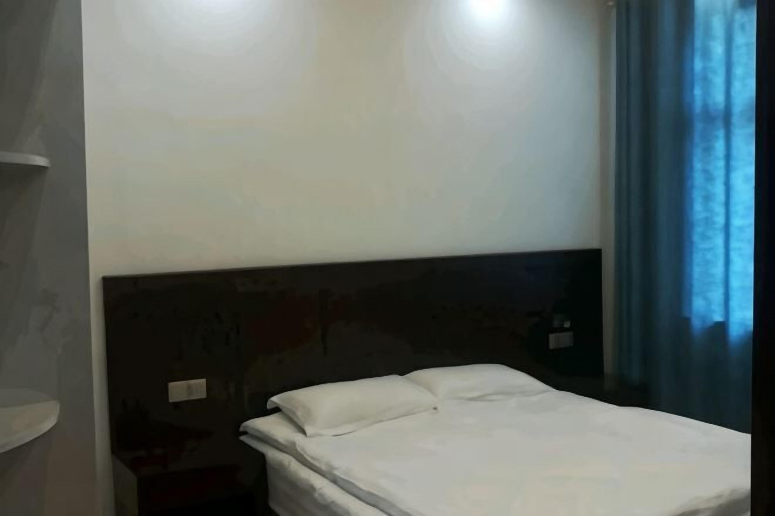 A hotel room with a bed, a nightstand, and a wall-mounted light fixture.