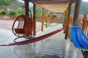 A hammock under a wooden pergola, a wicker swing chair, and a blue hammock on a wet concrete surface. - Baotianman Shanshui Inn (Neixiang)