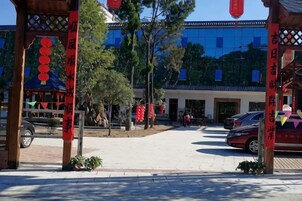Un patio con un pabellón tradicional, un edificio moderno al fondo y una zona de estacionamiento.