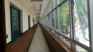 A corridor with large windows and doors, leading to a building with a view of trees and a blue structure outside. - Baotianman Shanshui Inn (Neixiang)