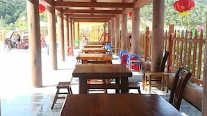 A covered outdoor seating area with wooden tables and chairs, a tiled floor, and a wooden fence with colorful decorations. - Baotianman Shanshui Inn (Neixiang)
