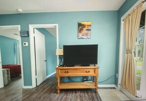 Una habitación con paredes color turquesa, un mueble de televisión de madera con televisor de pantalla plana, un cuadro sobre el televisor y una puerta que da a otra habitación.