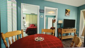 Um quarto com uma mesa de xadrez vermelha, cadeiras de madeira, uma televisão sobre um suporte de madeira e um letreiro na parede que diz "THE BEST DAYS ARE SPENT FISHING".