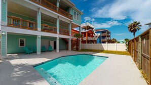A multi-story building with a swimming pool, outdoor seating, and a fenced yard. - Private Pool and Golf Cart Included (Port Aransas)
