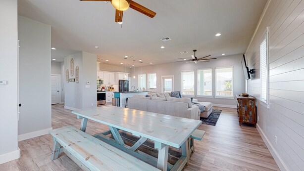A spacious living area with a large wooden table, a sofa, and a ceiling fan. - Private Pool and Golf Cart Included (Port Aransas)